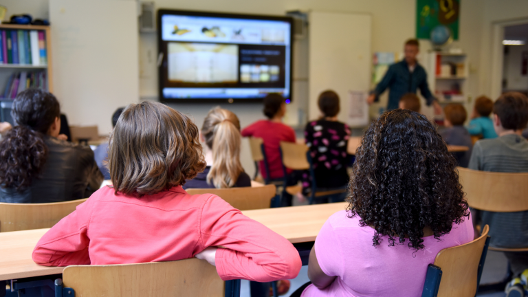 Élève en classe écoutant l’enseignant, qui donne son cours à l’aide d’outils numériques (tableau numérique).