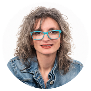 Portrait circulaire de Michèle Minor-Corriveau regardant la caméra, portant des lunettes turquoise et une veste en denim.